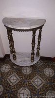 Front view of half moon hall table showing white marble top and shelf with three decorative brass legs.