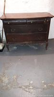 Full view of the vintage wooden dresser showing four drawers, curved legs, and decorative elements.