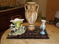 Three decorative vases displayed on a black textured cloth on a round table in a kitchen. Showcases size difference and detailed designs.