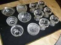 Top view showing all 11 assorted clear glass dessert bowls arranged on a black cloth on a light table surface.