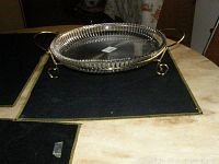 Round clear glass platter with textured diamond pattern on a gold metal stand with handles and curled legs, shown on a wooden surface.