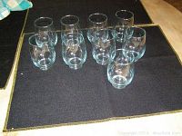 Eight clear stemless wine glasses arranged on a dark cloth showing shape, size and transparency.