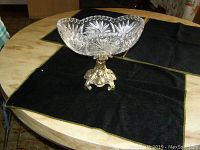 Full view of crystal bowl mounted on brass base on a round table with black cloth underneath.