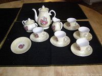 Front angle view of the children's porcelain tea set showing teapot, sugar bowl, creamer, cups, saucers, and plate on a black cloth background.