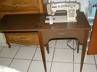 Photo of vintage zig zag sewing machine integrated into wooden cabinet with storage drawers, showcasing sewing area and cabinet legs.