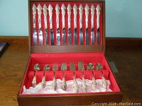 Full view of the wooden red-lined box containing silver plated cutlery including 12 knives in the lid section, and 12 forks and 12 spoons in the base section, all with ornate floral decorated handles.