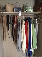 Photo showing hanging women's sweaters and coats in colors including gray, white, red, blue, green, beige with several belts hanging to the left and three purses on the top shelf.
