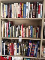 Three shelves filled with various books in multiple genres and conditions.