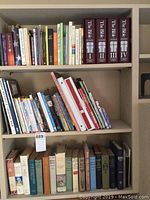 Three shelves of assorted books including novels, reference, and the Bible on cassette