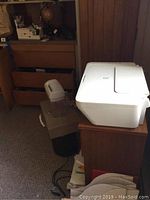 White Canon Pixma MG-2520 printer on wooden cart with drawer, small white paper shredder and black trash bin beneath, additional papers and supplies visible.