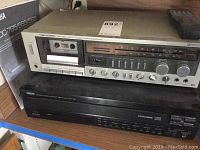 Silver-tone Realistic cassette receiver with multiple control knobs and cassette slot. Partial view of Yamaha CD player below it.