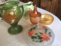 Lot overview showing multiple collectible pottery and glass pieces on a table.