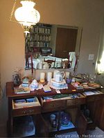 Full view of sideboard with glassware, candles, Wedgwood, linens on top and inside drawers and cabinets, plus hanging Gone With The Wind style lamp above.