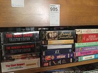 Shelf displaying various VHS tapes horizontally, featuring titles like The Lucy Show Collector's Edition, E.T., Frank Sinatra Presents, Fiddler on the Roof, Barney, and Civil War.