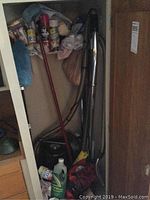 Closet area showing the Rainbow air cleaner hose, Dirt Devil vacuum, various cleaning products and tools packed inside a small closet space.