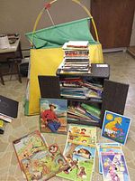 Stack of varied children's books and puzzles in a woven basket with yellow and green play tent behind them.