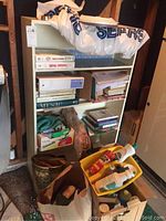 Photo showing white bookcase loaded with books, binders, and cleaning supplies placed on floor and shelf