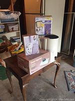 Three small home electronics in packaging or assembled on an occasional table with storage boxes visible in the background