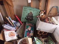 Photo showing an assortment of Christmas and holiday items including a box labeled '40 Musical Bell Lights in Motion,' holiday wrapping paper, tins, a plush reindeer, and various decorative items.