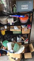 Five shelves filled with assorted vintage and classic kitchen utensils and appliances including boxed food chopper, blender, salad spinner, vintage Tupperware, electric wok, bread box, and more.