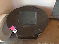 Top view of round vintage Pong arcade game table showing dark tabletop with central screen display.