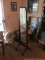 Full view of vintage floor mirror showing the carved top and wooden stand with four legs.