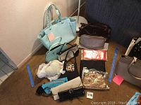 Photo showing assortment of women's small handbags and evening purses on floor including a large light blue BCBG tote bag with studded handles, smaller purses in multiple colors and materials.