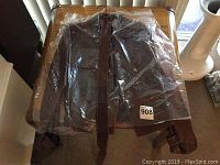 Brown women's leather jacket in plastic protective covering, displayed on a chair.