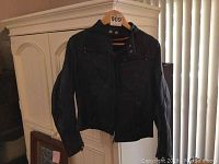 Full view of black women's leather jacket on hanger, showing overall design and fit.