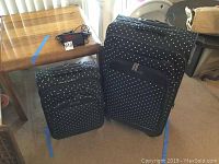 Photo showing two black fabric suitcases with white polka dots, one larger and one smaller, with a Garmin GPS device charger on top of a wooden table.