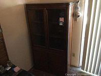 Front view of closed wooden cabinet with glass doors on upper section and solid doors on bottom.