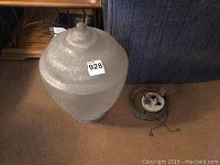 Side view of the textured clear glass lamp globe with mounting ring and attached wiring on carpeted floor.