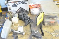 Overall view of the lot showing Black and Decker cordless drill in box, circular saw, Stanley Mitre Box, clear plastic storage boxes with hardware, string, various tools, and accessories on workbench.