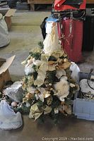 Small decorated Christmas tree showing gold and white floral ribbons and white angel topper