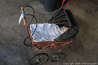 Side angle view of the vintage doll pram showing the orange metal frame, black fabric canopy, lace interior lining, and wheels.