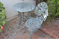 Full view of the metal round table and chair showing detailed rose patterned design and condition