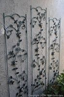 Three metal rose-themed wall panels with decorative vine and leaf designs shown against a textured wall.