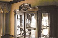 Front upper view of wooden china hutch with glass doors and carved top detail.