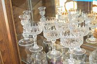 Photo showing 6 clear crystal stemware glasses with detailed cut patterns on short stems displayed on glass shelf with mirrored background.