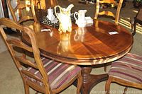 Dining table and one wooden chair with striped cushion seat showing wood grain and polished surface under indoor light.