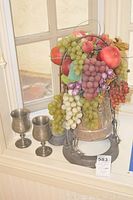 Full view of pewter coffee urn with ceramic fruit bowl on top and two pewter goblets beside it