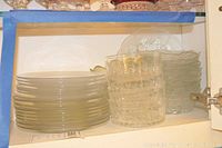 Shelf containing stacked clear glass plates on the left, several clear dessert bowls in front, and clear salad bowls behind.