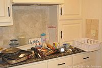 Kitchen counter with various trays, utensils, containers, and kitchen items spread out.