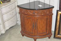 Front view of wooden corner cabinet with black stone top and decorative carved drawer and door fronts