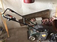 Side view of Black and Decker electric lawnmower with green deck and black flip-over handle, showing power cord and wheels.