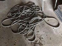 Coiled metal garden hose lying on a concrete floor, showing the length and metallic construction of the hose.