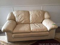 Front view of beige loveseat showing two leather seat cushions, padded armrests, and faux leather back and sides.
