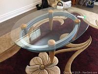 Oval glass-topped coffee table with wooden legs from above, showing the clear glass and quality finish on wood.
