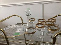 Glass decanter with gold-colored band and six matching wine glasses on a gold-tone metal and glass tray.