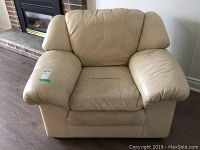 Full view of the beige leather armchair showing cushioned seat, armrests, and backrest in a living room setting.